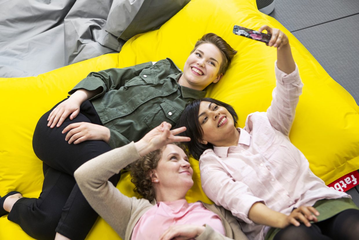 Kolme opiskelijaa makoilee säkkituoleilla. Yksi ottaa ryhmästä selfien.