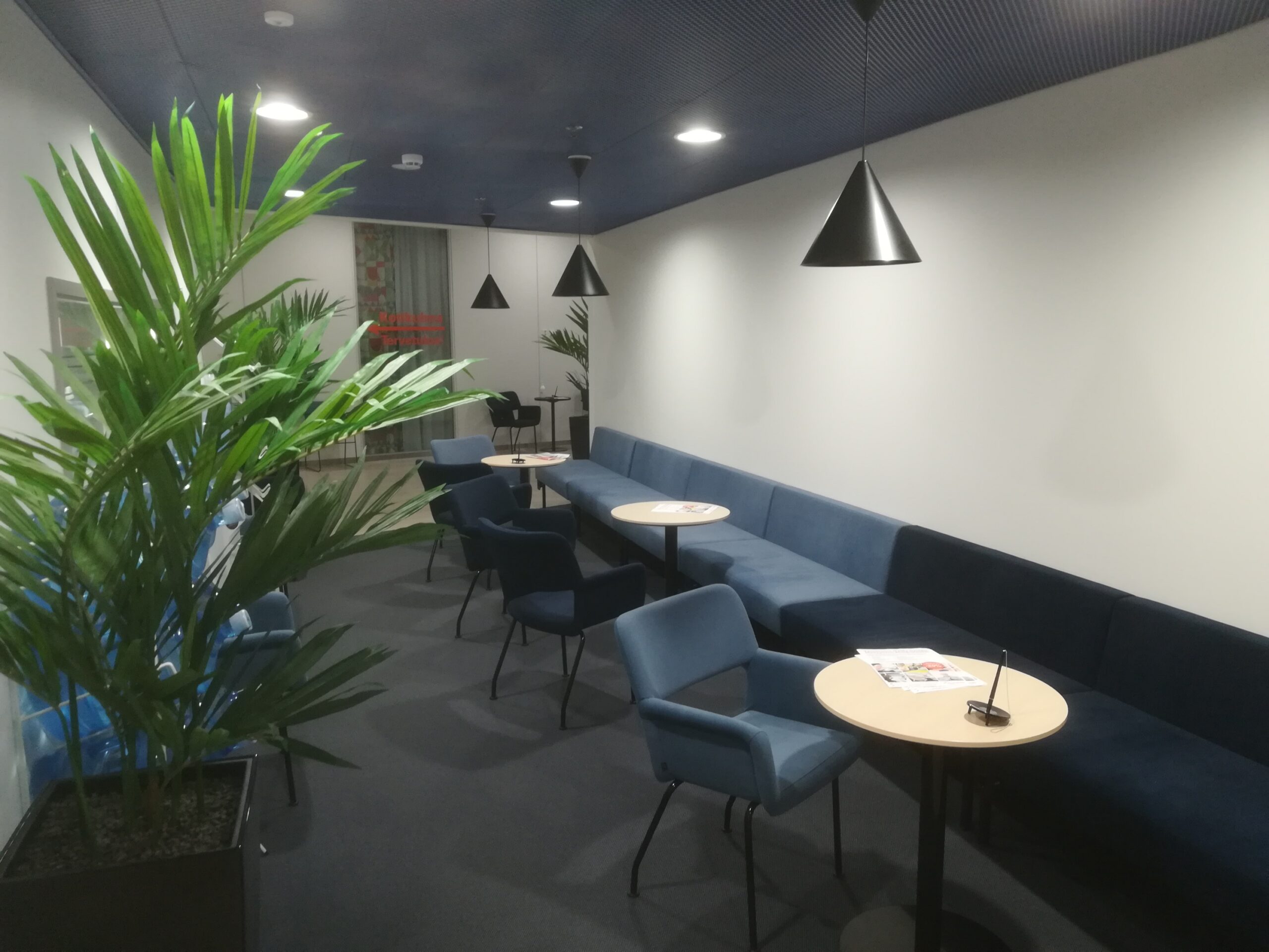 HyMy-kylän aulassa on pitkä sohva vaaleaa seinää vasten, kolme pientä pyöreää pöytää, nojatuoleja sekä viherkasveja.svi