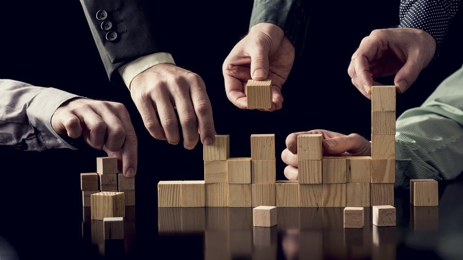 Four hands moving wooden building blocks on black table.