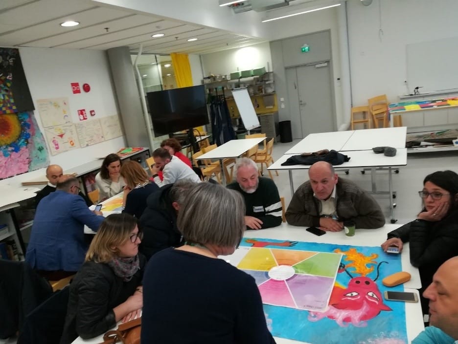 People are sitting in a classroom at Metropolia UAS during a collaboration workshop. They are working in small groups discussing, co-creating and developing new services together.