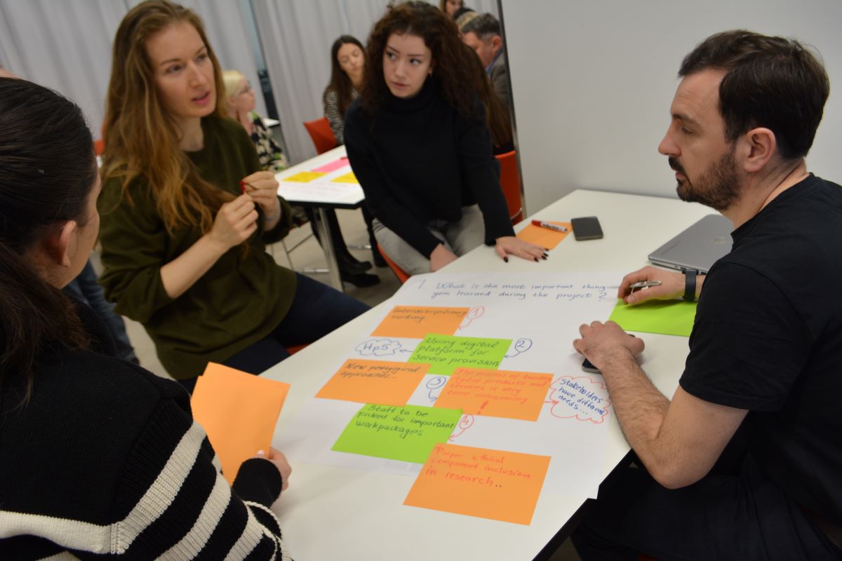Students seated around a table, post it notes on it.