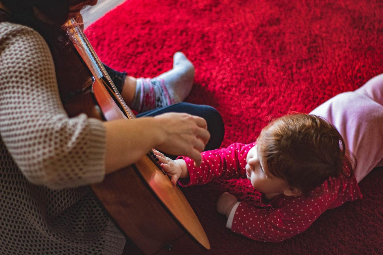 Lapsi kitaran luona: Kuvassa pieni musiikkiryhmän osallistuja on ryöminyt koskettamaan ryhmänohjaajan kitaraa