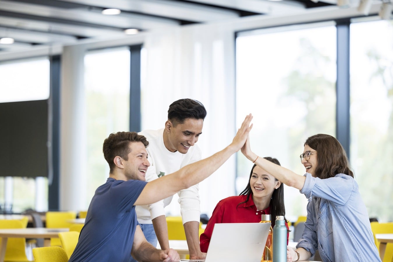 Neljä nuorta ihmistä oppilaitoksen pöydän ympärillä, kaksi mies- ja kaksi naisoletettua. Etualalla olevat mies ja nainen heittävät ylävitoset.