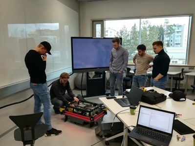 Viisi henkilöä katselee luokkahuoneessa MiR100 robottia.