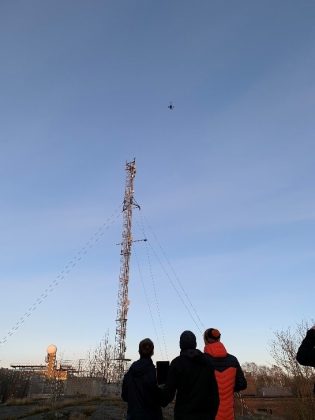 Kolme ihmistä katselevat ulkona droonin lentoa.