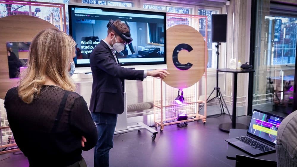 Nainen seisoo selin kameraan ja katsoo, kun mies kokeilee virtuaalilaseja