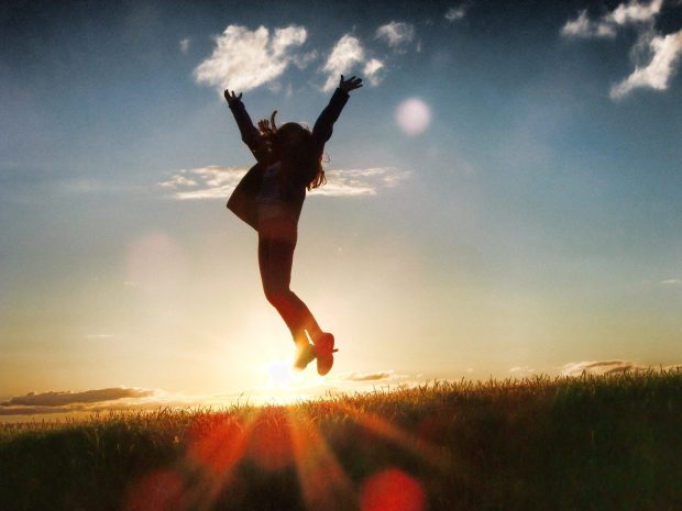 siluetti henkilöstä joka hyppää korkealle ilmaan, taustalla auringonnousu ja taivasta