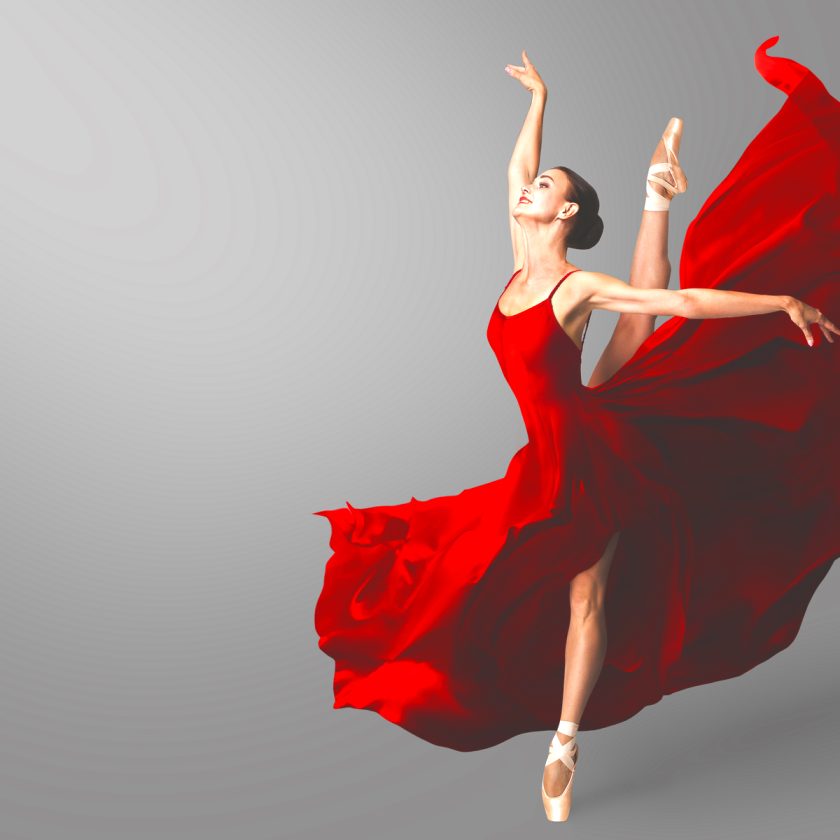 Ballerina seisoo yhdellä jalalla sivuprofiilissa kärkitossuilla punaisessa hulmuavassa mekossa, kädet avoinna katse ylöspäin