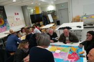 People are sitting in a classroom at Metropolia UAS during a collaboration workshop. They are working in small groups discussing, co-creating and developing new services together.