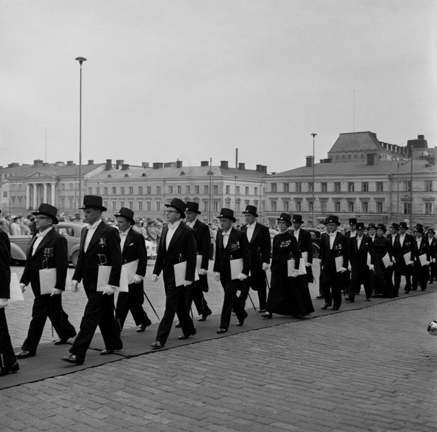 Mustavalkoinen kuva vuodelta 1957, hattupäisiä tohtoreita kävelemässä Senaatintorilla jonossa.