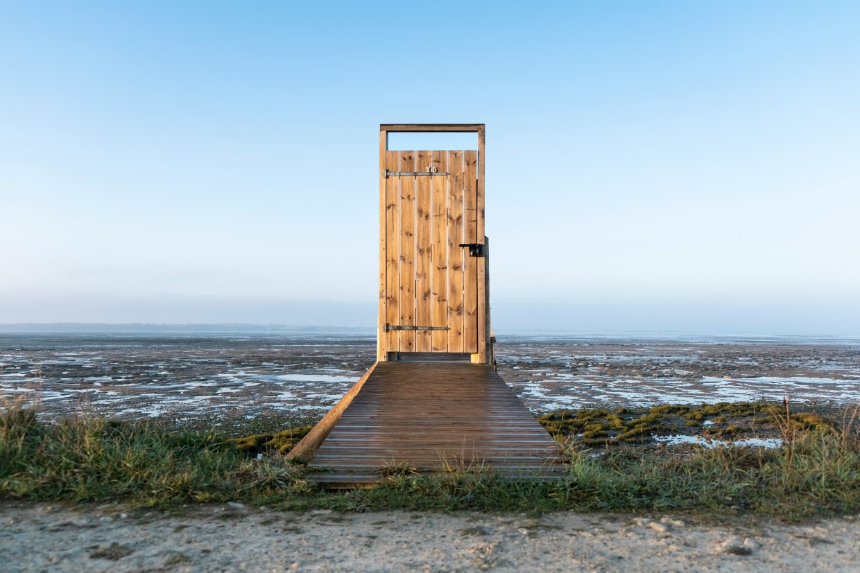 A view from beach to sea, in the middle wooden pier, at the end of pier a wooden door.