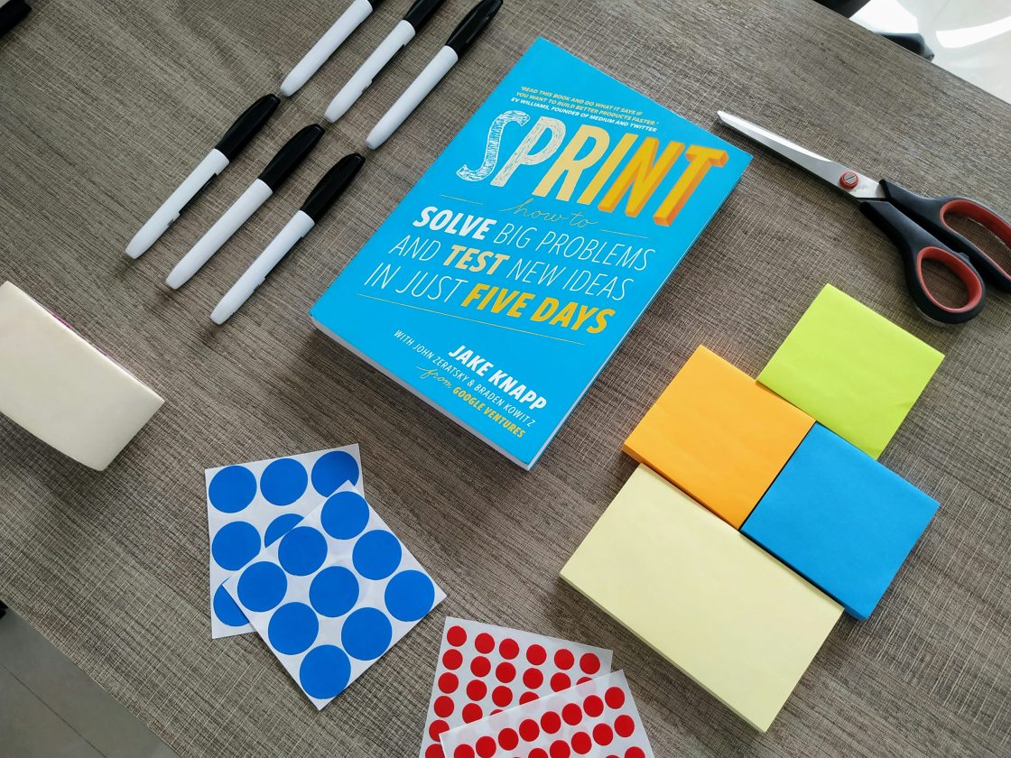 Postit-notes stacked on table, along with a book on Sprint, and possibly pencils.