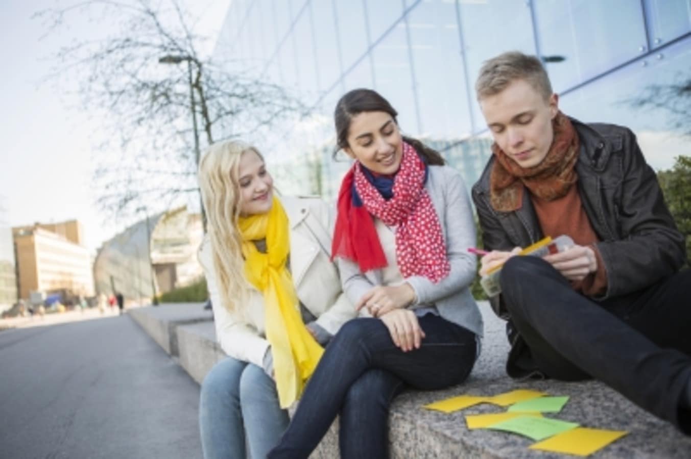 Kolme ihmistä istuvat ulkona ja työskentelevät yhdessä hyödyntäen post-it-lappuja.