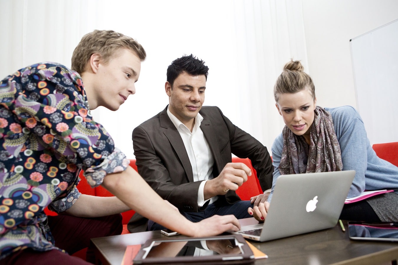 http://Kolme%20henkilöä%20istuu%20rinnakkain%20työpöydän%20äärellä,%20katsovat%20keskimmäisen%20edessä%20avoinna%20olevan%20läppärin%20ruutua.