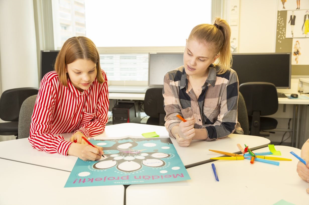 Luokkahuone, kaksi kouluikäistä lasta istuu rinnakkain, pöydällä juliste.