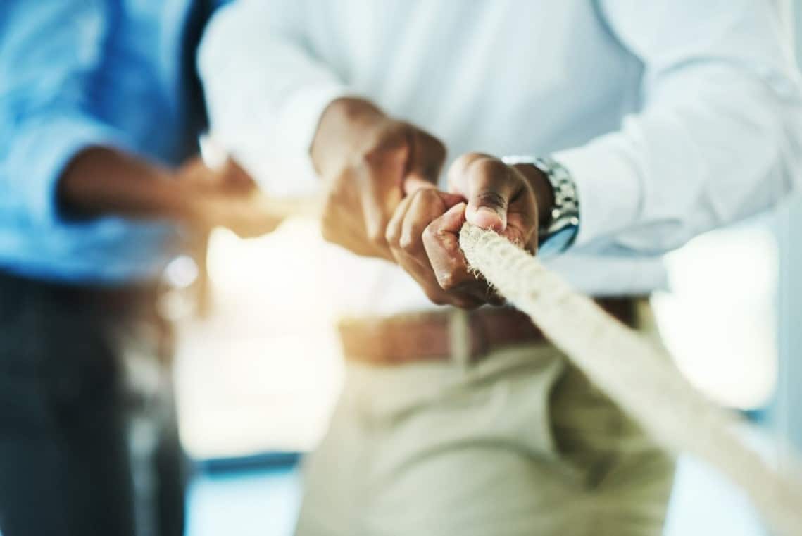 Miehen kädet vetävät köyttä, taustalla on toinen hahmo vetämässä myös köyttä.