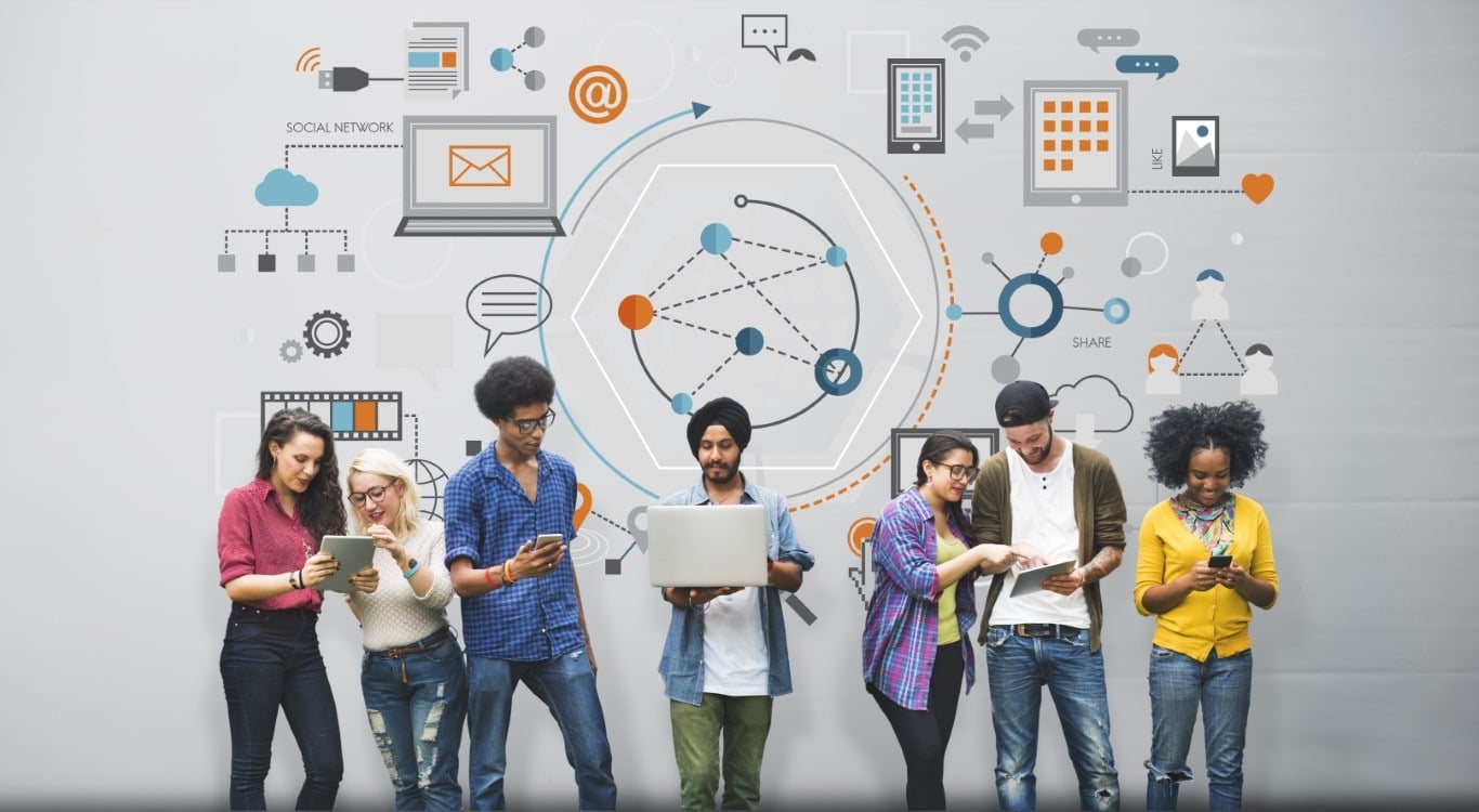 Nuoria henkilöitä nojailee rivissä seinään, keskimmäisellä läppäri kädessä, seinässä graafisia kuvioita.