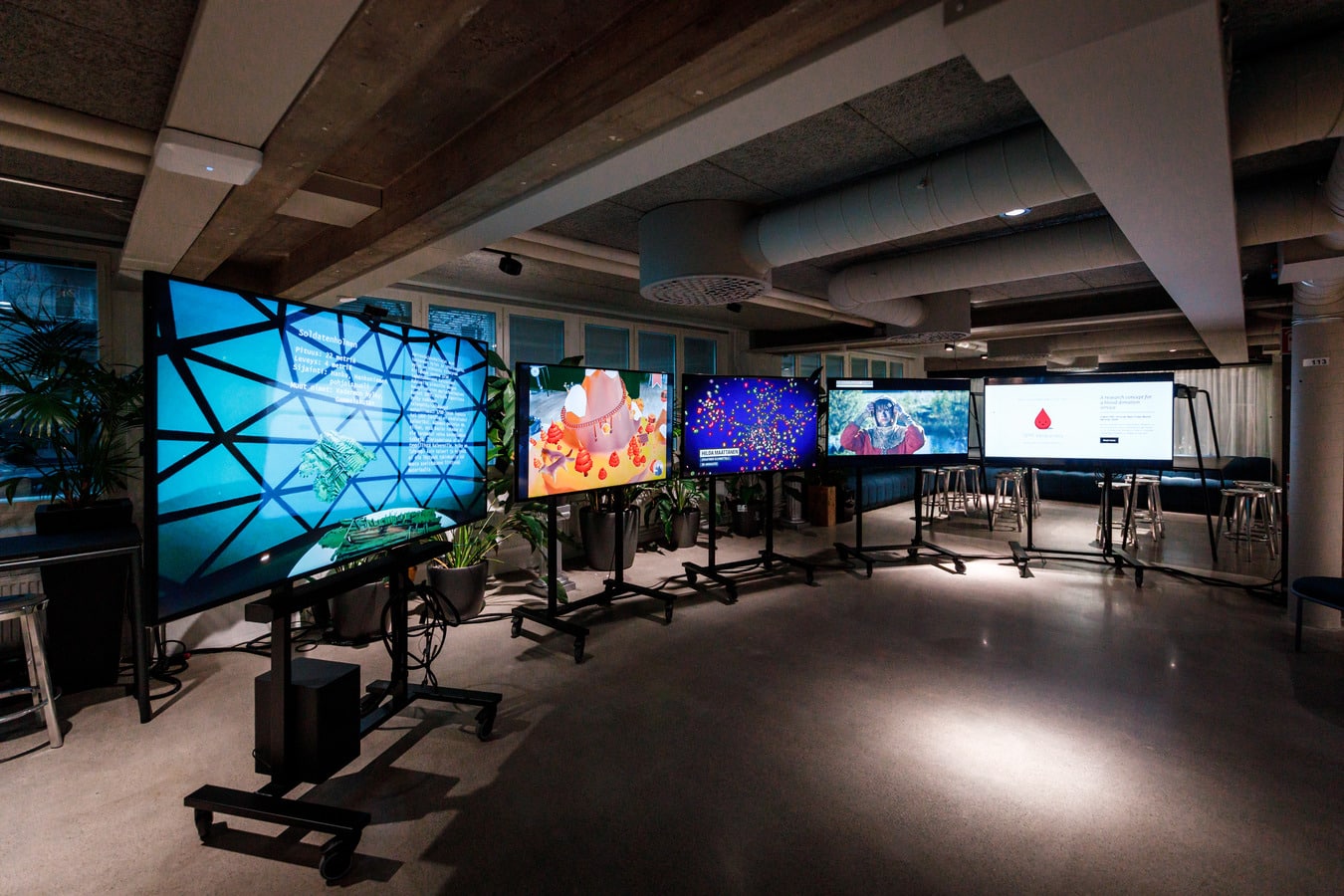 Pimeässä huoneessa televisioruutuja rinnakkain kaaressa, jalustoilla.