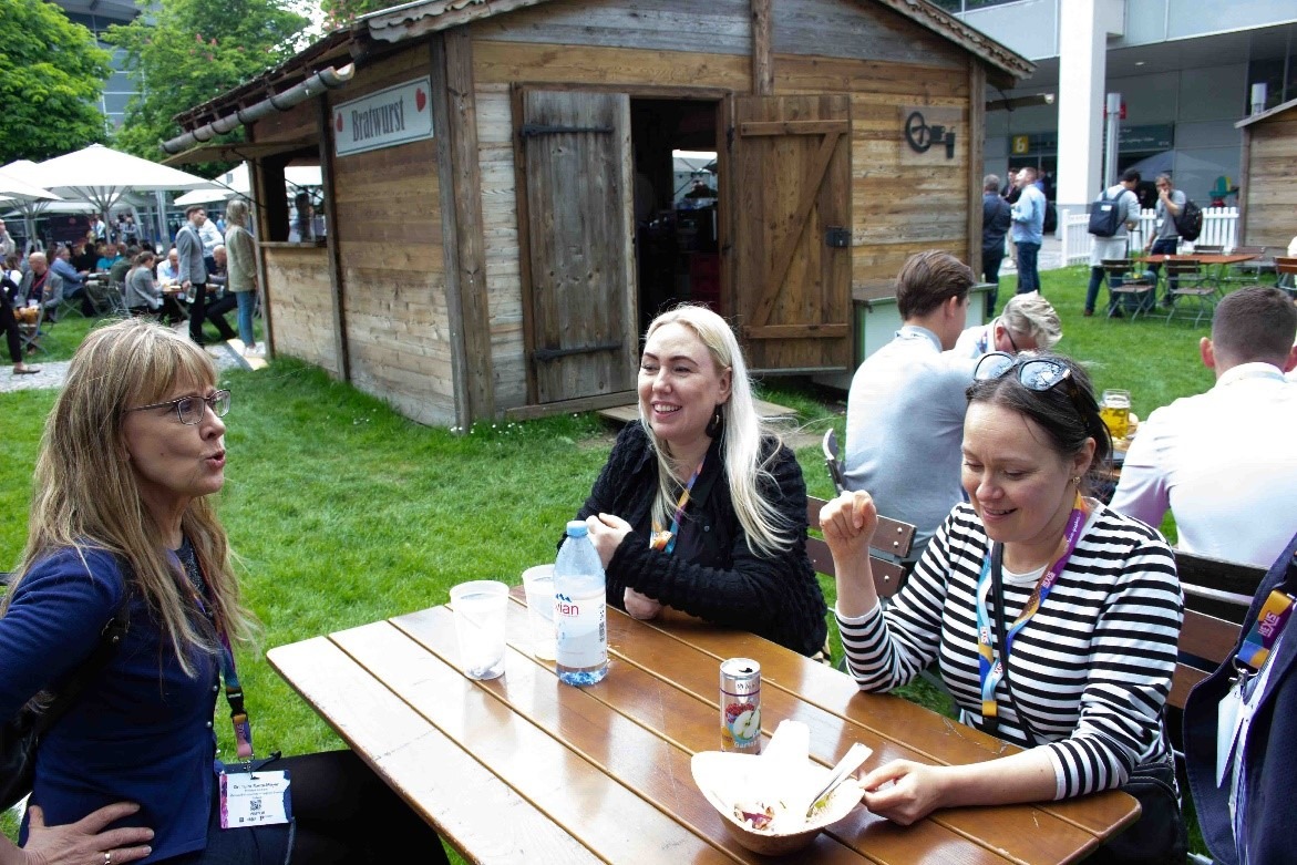 Kuvassa osallistujat istuvat messualueella sijainneen Bratwurst-kojun pöydän ääressä lounaalla.