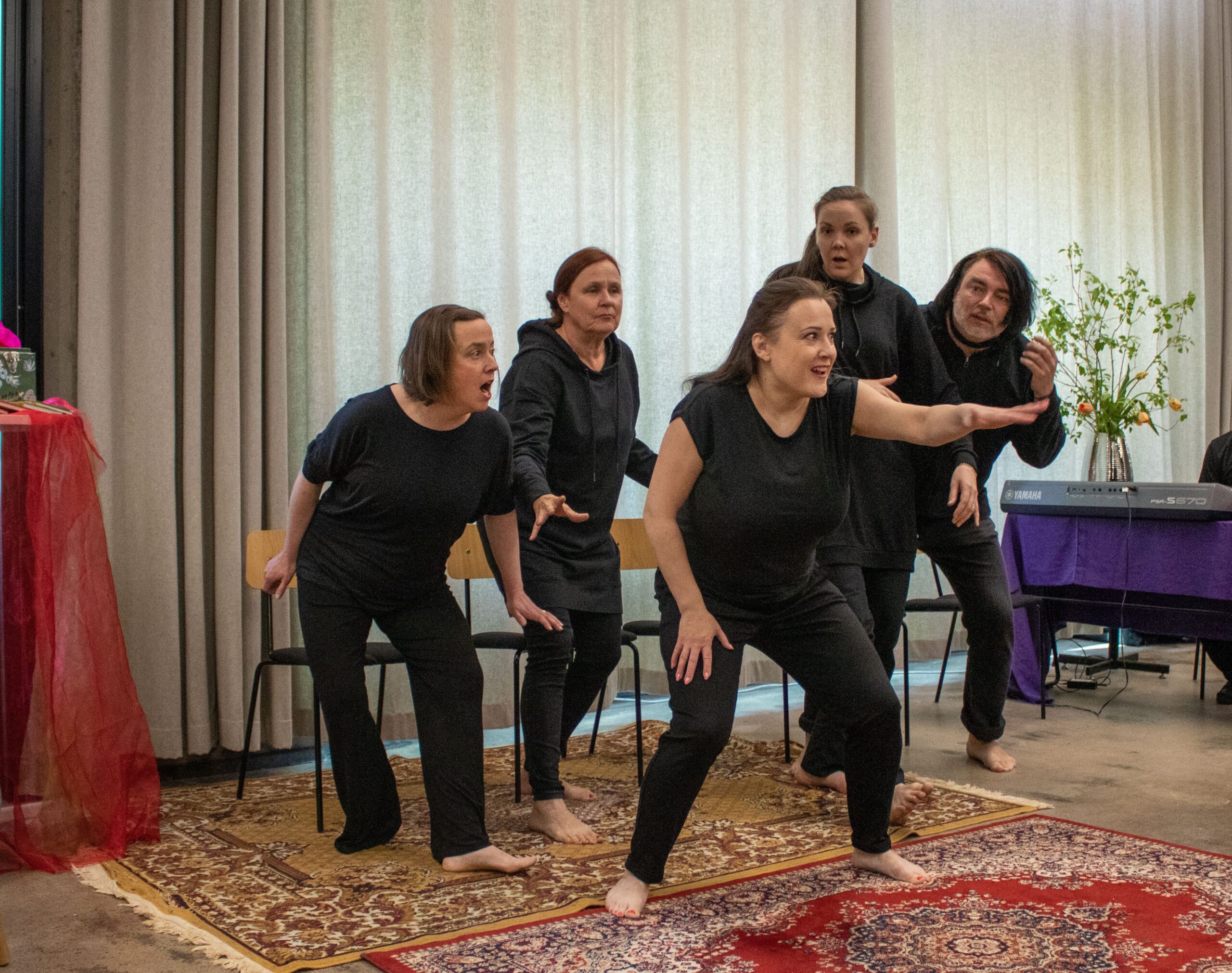 Tarinateatteriesitys. Viisi henkilöä mustissa vaatteissa ilmikkäänä, etualalla oleva osoittaa kädellä kohti yleisöä. 